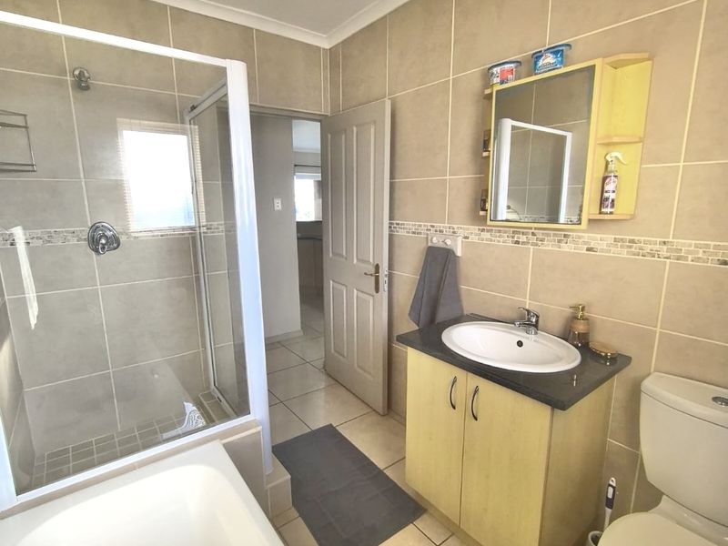 A functional bathroom featuring a shower enclosure, bathtub, vanity cabinet with basin, and toilet, finished with neutral wall and floor tiles.