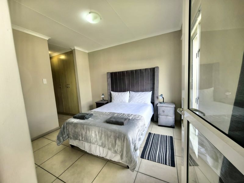 A well-maintained bedroom featuring tiled flooring, built-in cupboards, and direct access to an outdoor area through a glass sliding door.