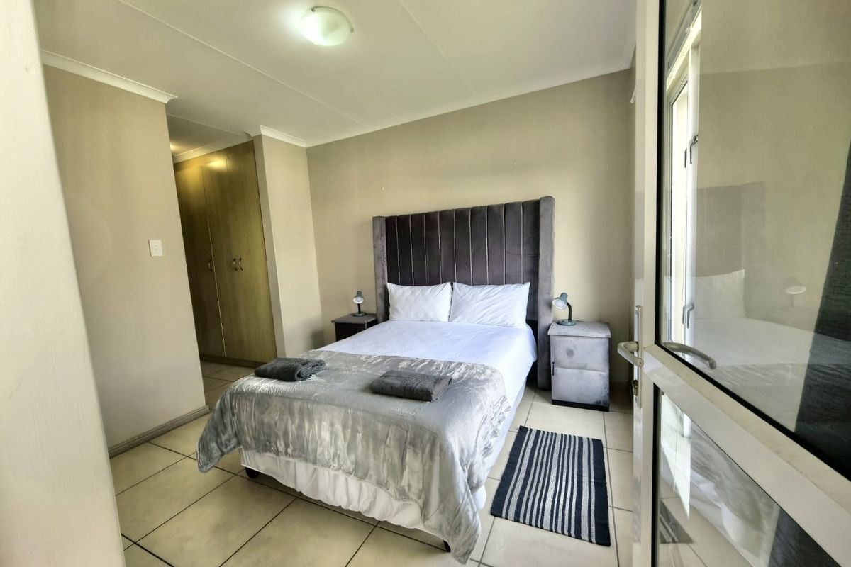 A well-maintained bedroom featuring tiled flooring, built-in cupboards, and direct access to an outdoor area through a glass sliding door.