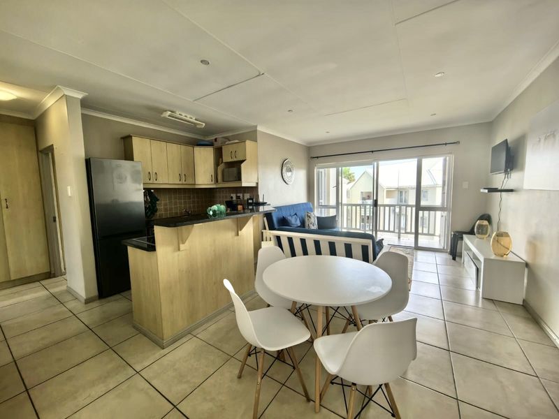 Open-plan living and dining area featuring tiled floors, a functional kitchen with breakfast bar, and sliding doors leading to a balcony.