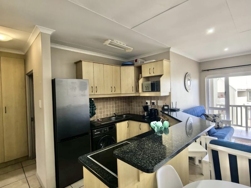 Open-plan kitchen and living area featuring granite countertops, tiled backsplash, and direct access to a balcony through sliding glass doors.
