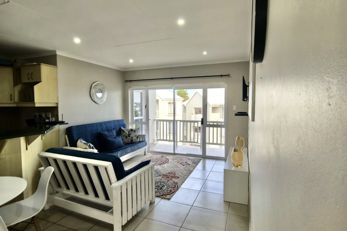 Open-plan living area featuring tiled floors, recessed lighting, and direct access to a balcony through sliding glass doors, adjacent to a compact kitchen.