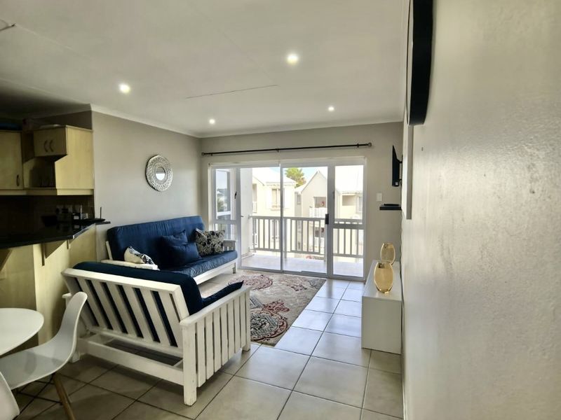 Open-plan living area featuring tiled floors, recessed lighting, and direct access to a balcony through sliding glass doors, adjacent to a compact kitchen.