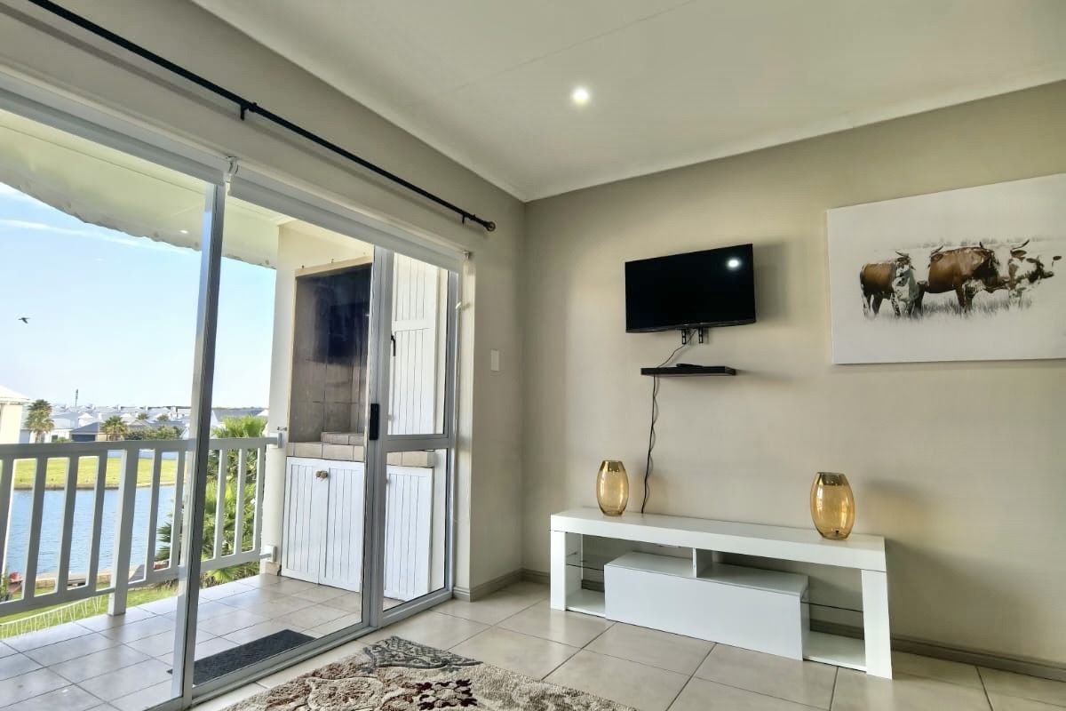 A bright living room featuring tiled floors, recessed lighting, and a sliding door leading to a balcony with a built-in braai.