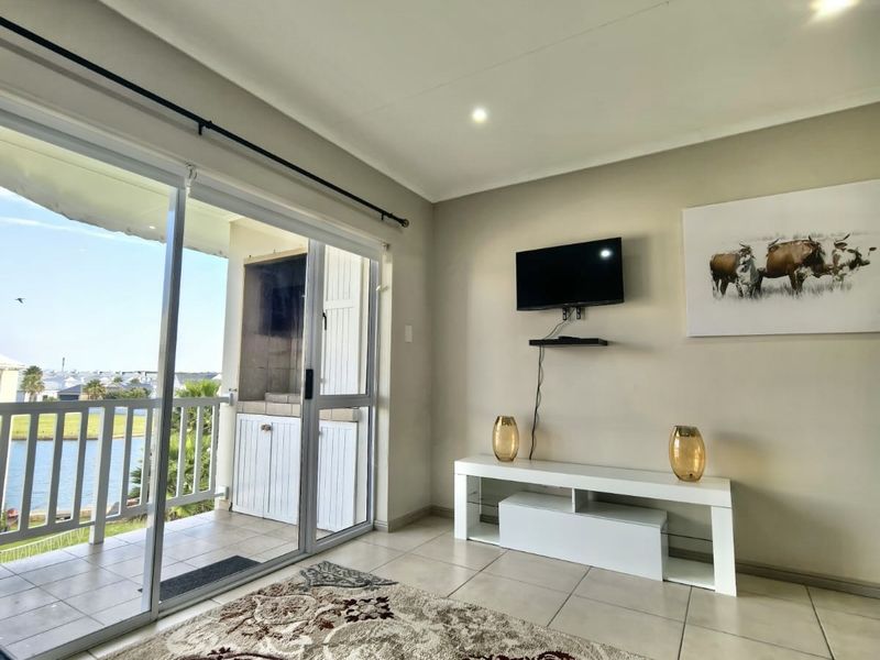 A bright living room featuring tiled floors, recessed lighting, and a sliding door leading to a balcony with a built-in braai.