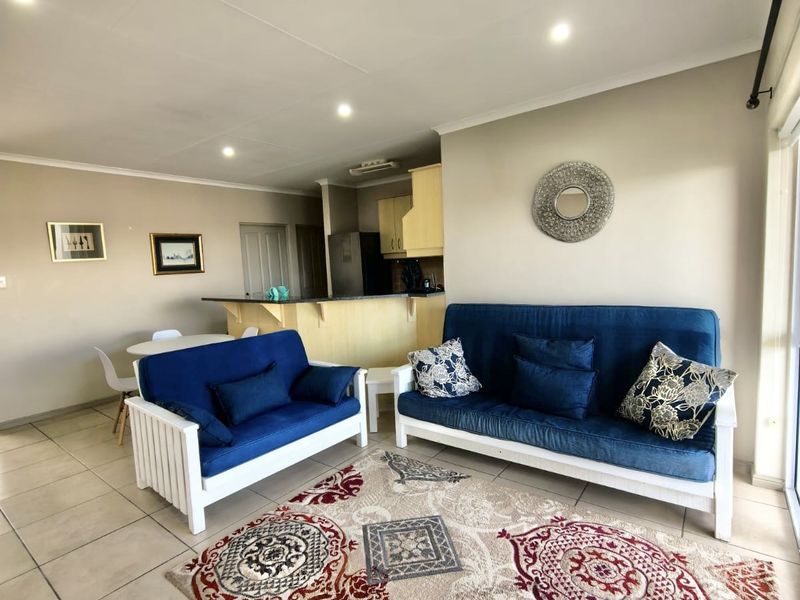 Open-plan living and dining area featuring tiled flooring, recessed lighting, and a functional kitchen with a breakfast bar, leading to a sliding glass door.