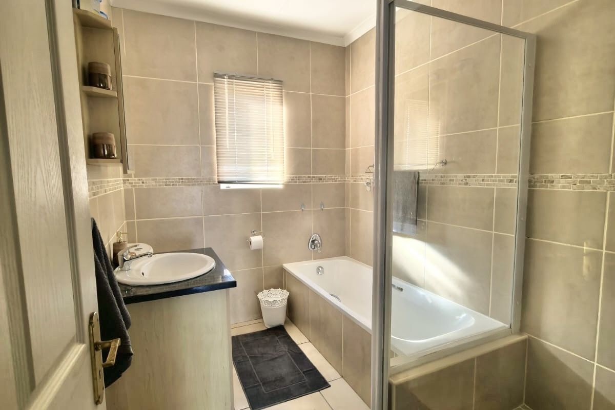 A well-maintained bathroom featuring a built-in vanity, a bathtub, and a separate glass-enclosed shower with neutral wall and floor tiling.