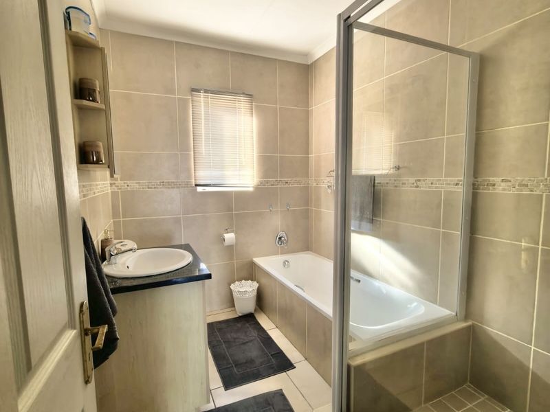 A well-maintained bathroom featuring a built-in vanity, a bathtub, and a separate glass-enclosed shower with neutral wall and floor tiling.