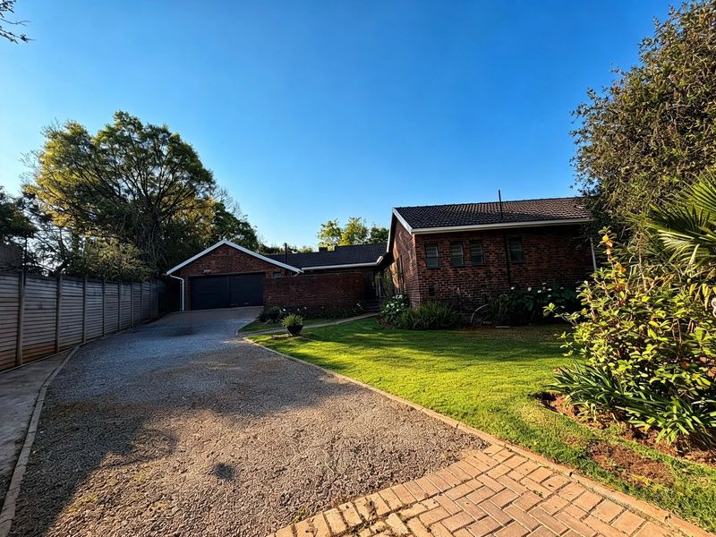 Front view of a brick house featuring a double garage, gravel driveway, and well-maintained garden area.
