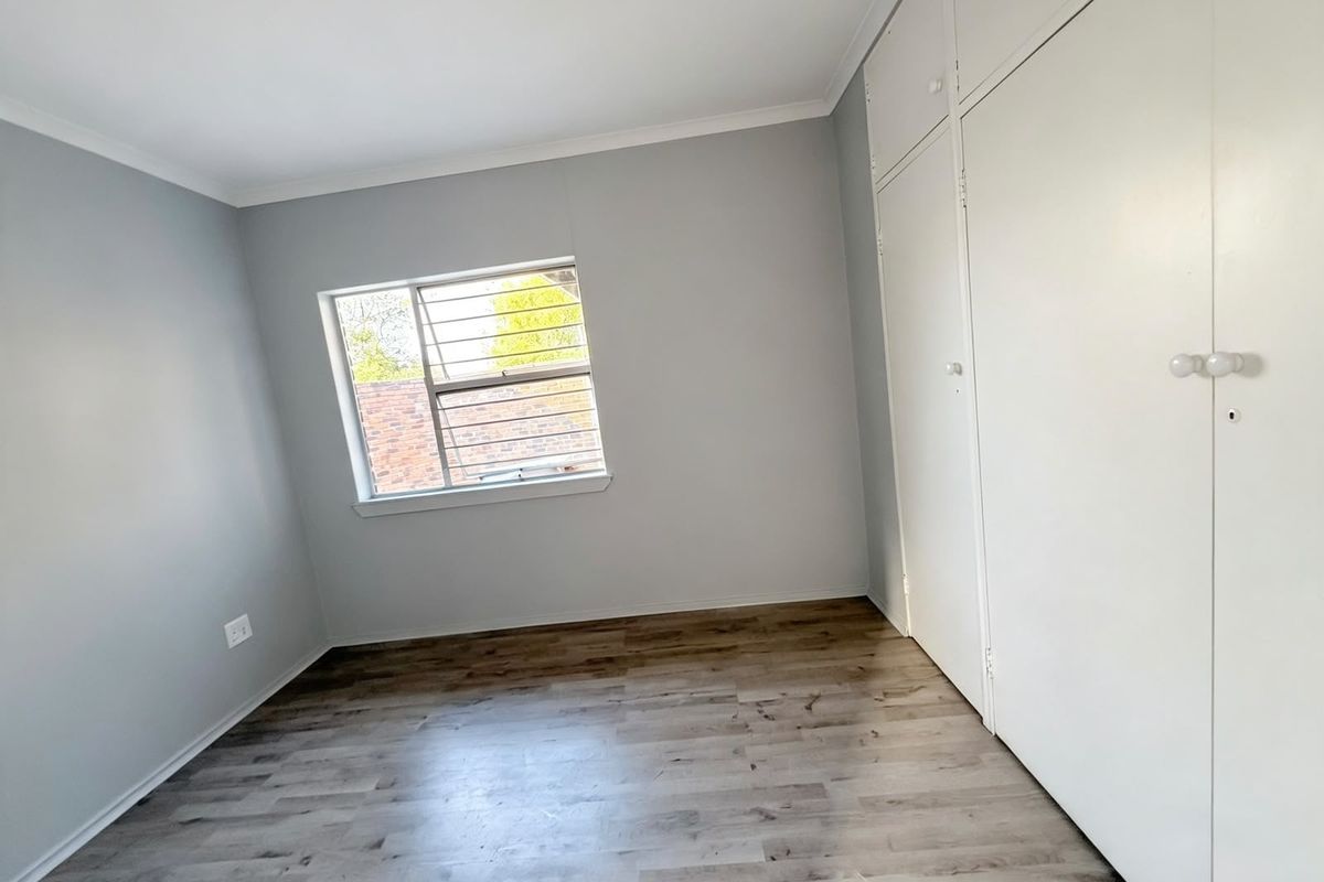 A bright, empty bedroom featuring modern grey laminate flooring, neutral walls, and built-in storage cupboards.