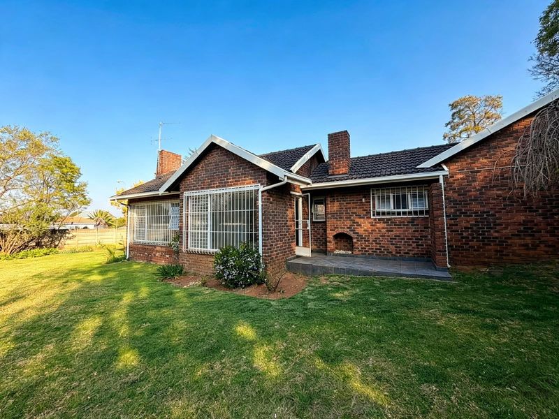 Rear view of a brick house featuring a tiled roof, security bars on windows, and a built-in outdoor fireplace on a paved patio area.
