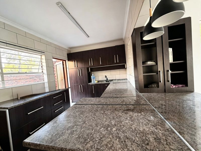 A clean, functional kitchen featuring dark wood cabinetry, stone-look laminate countertops, tiled backsplash, and ample storage space with integrated lighting.