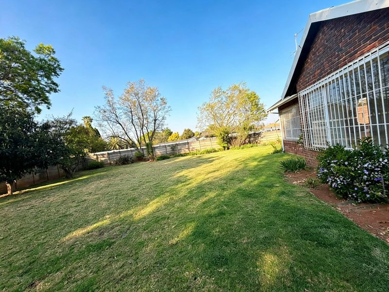 A spacious rear garden featuring a well-maintained lawn, established trees, and a secure brick-walled perimeter.