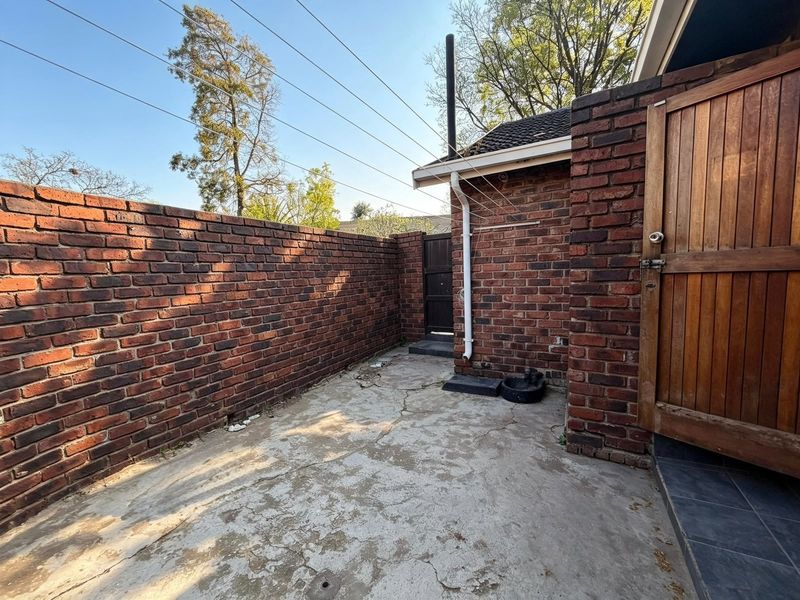 A private rear courtyard area featuring brick boundary walls, concrete paving, and a timber access gate.