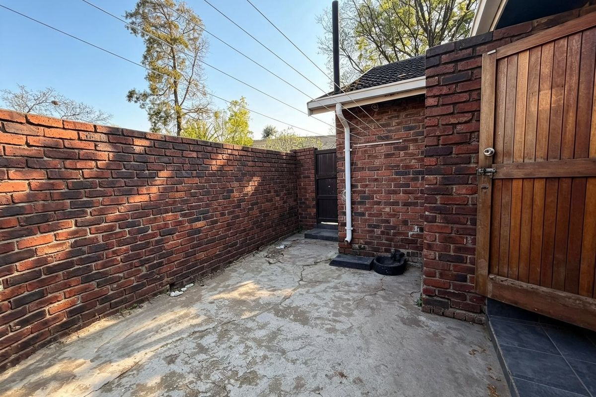 A private rear courtyard area featuring brick boundary walls, concrete paving, and a timber access gate.