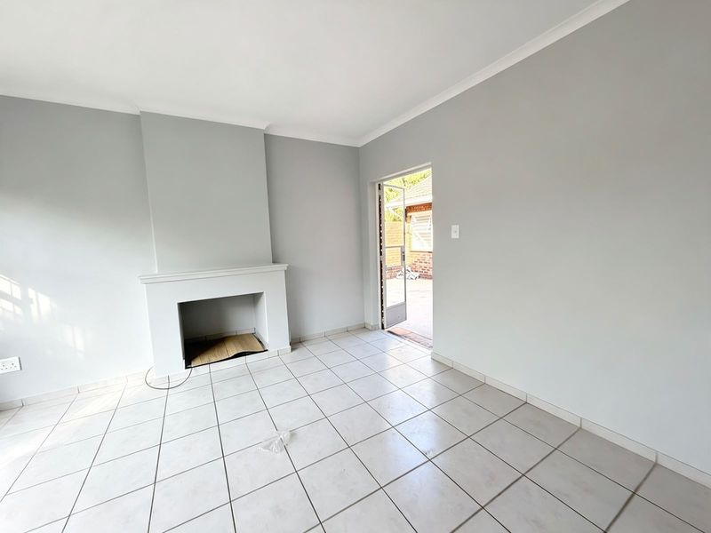 A bright, empty living room featuring neutral walls, tiled flooring, and a built-in fireplace, with direct access to the outdoor area.