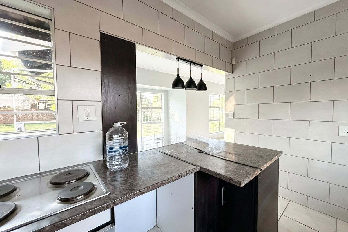Kitchen area featuring tiled walls, laminate countertops, and a built-in electric hob, with an open-plan layout connecting to the adjacent living space.