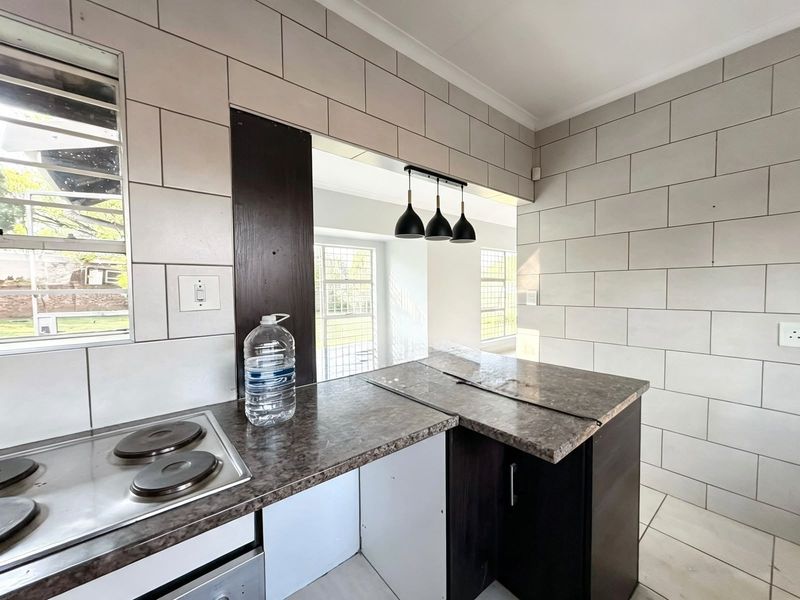 Kitchen area featuring tiled walls, laminate countertops, and a built-in electric hob, with an open-plan layout connecting to the adjacent living space.
