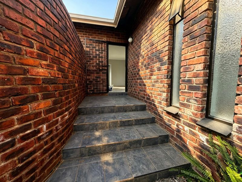 An exterior entrance featuring a tiled staircase leading to a doorway, framed by exposed brick walls and modern security gate.