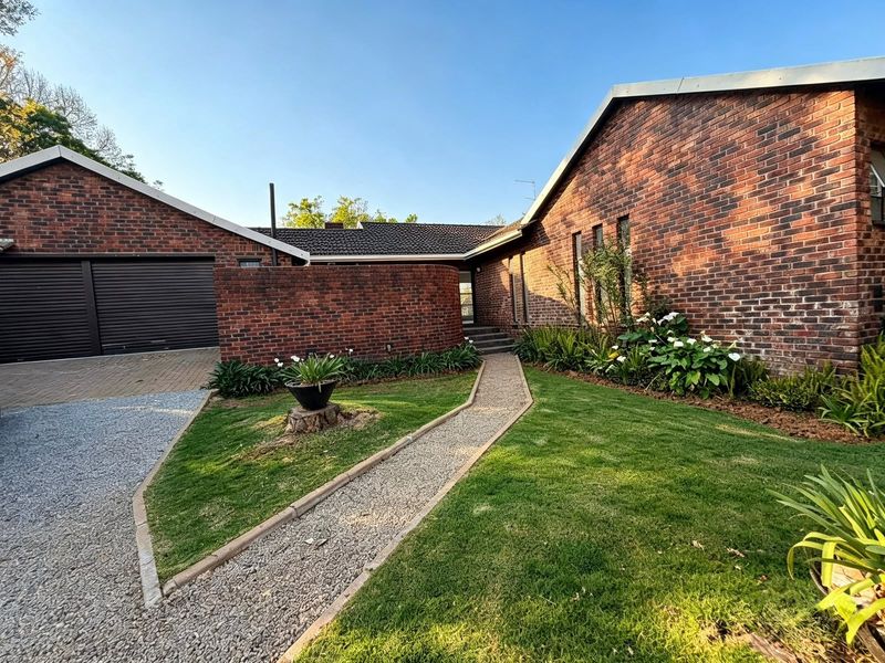 Front view of a well-maintained brick house featuring a double garage, paved walkway, and landscaped garden area.