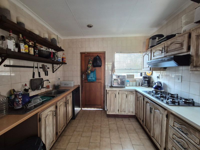 A functional kitchen featuring built-in cabinetry, a gas hob with extractor fan, double sink, and tiled finishes throughout.