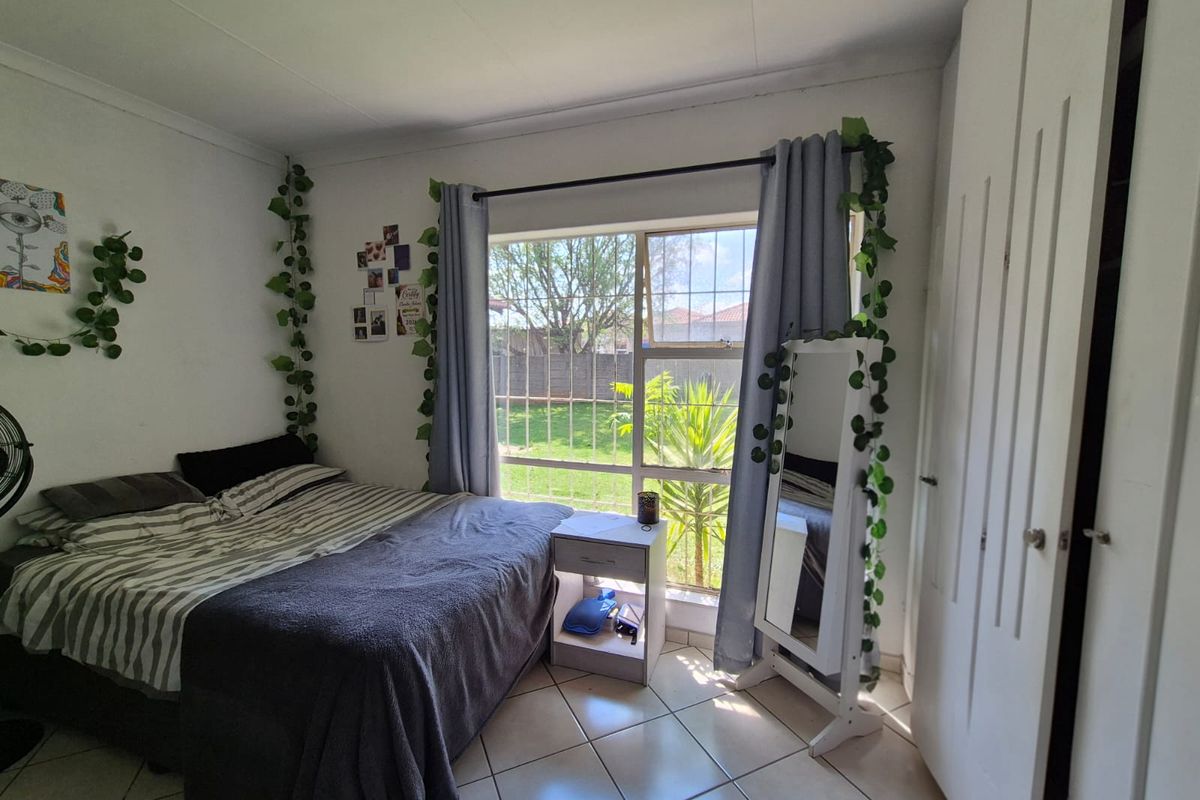A bedroom featuring tiled flooring, a built-in wardrobe, and a large window with security bars overlooking the garden.