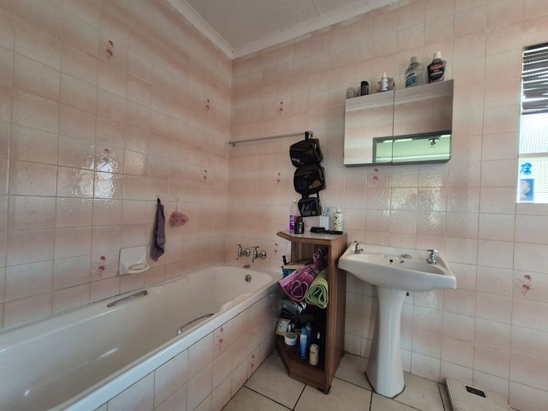 A functional bathroom featuring a standard bathtub, pedestal washbasin, and wall-mounted medicine cabinet, finished with dated ceramic wall and floor tiles.