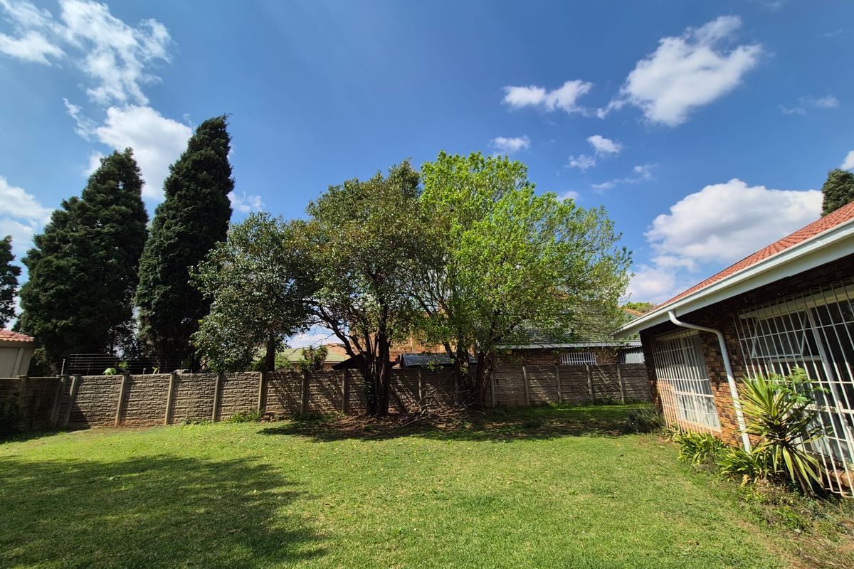 A spacious rear garden featuring a well-maintained lawn, mature trees, and a secure precast concrete boundary wall.