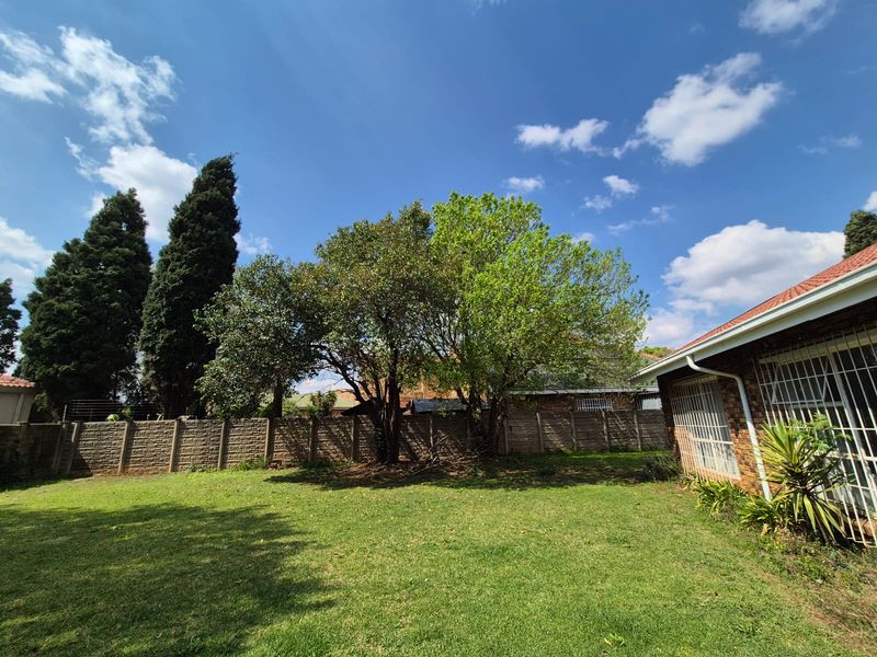 A spacious rear garden featuring a well-maintained lawn, mature trees, and a secure precast concrete boundary wall.