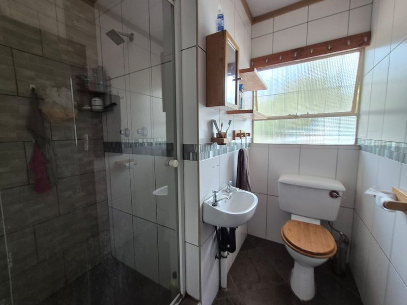 A functional bathroom featuring a shower enclosure, wall-mounted basin, and toilet with tiled finishes and natural light from an obscured glass window.