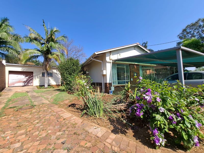 Front exterior view of the house featuring a brick driveway, a carport, and a separate detached garage set within a landscaped garden.