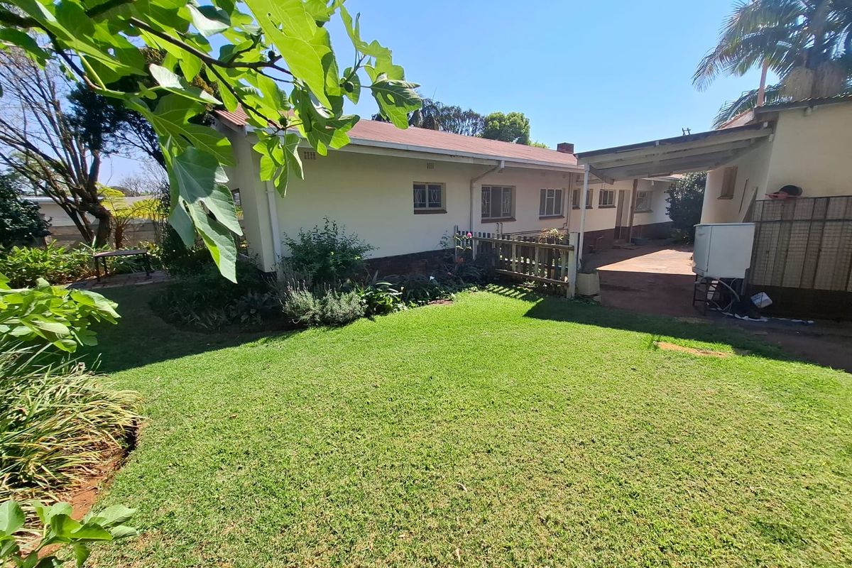 A view of the rear exterior of the house featuring a well-maintained lawn, a covered patio area, and established garden landscaping.