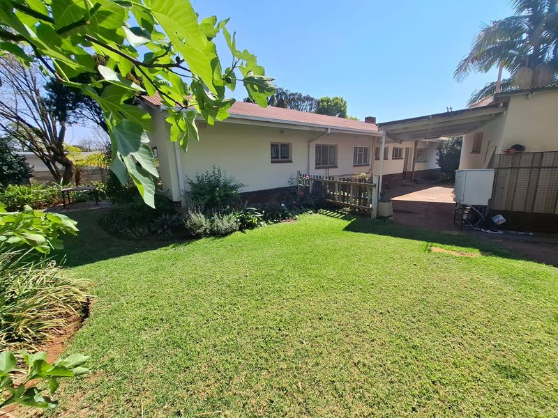 A view of the rear exterior of the house featuring a well-maintained lawn, a covered patio area, and established garden landscaping.