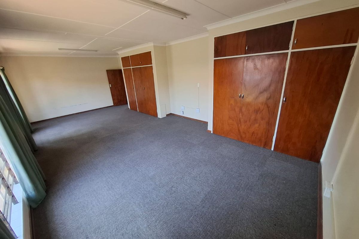 Spacious bedroom featuring extensive built-in wooden cupboards, neutral walls, and carpeted flooring, offering a blank canvas for renovation.