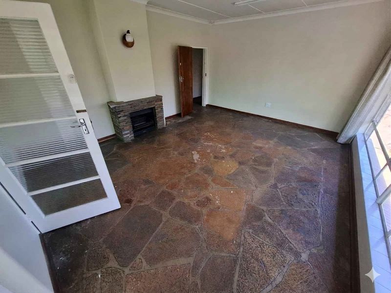 An empty living room featuring a stone fireplace, unique flagstone flooring, and a classic french door entrance.