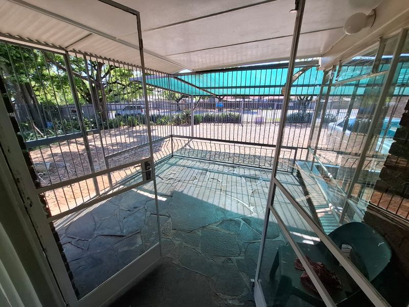 A covered outdoor patio area featuring stone paving and extensive metal security screening, providing a secure transition space to the front garden.
