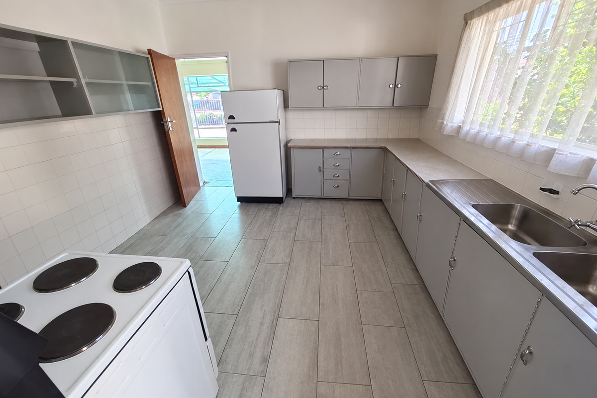 A functional kitchen featuring grey cabinetry, tiled splashbacks, a double stainless steel sink, and tiled flooring, with direct access to an outdoor area.