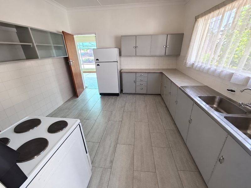 A functional kitchen featuring grey cabinetry, tiled splashbacks, a double stainless steel sink, and tiled flooring, with direct access to an outdoor area.