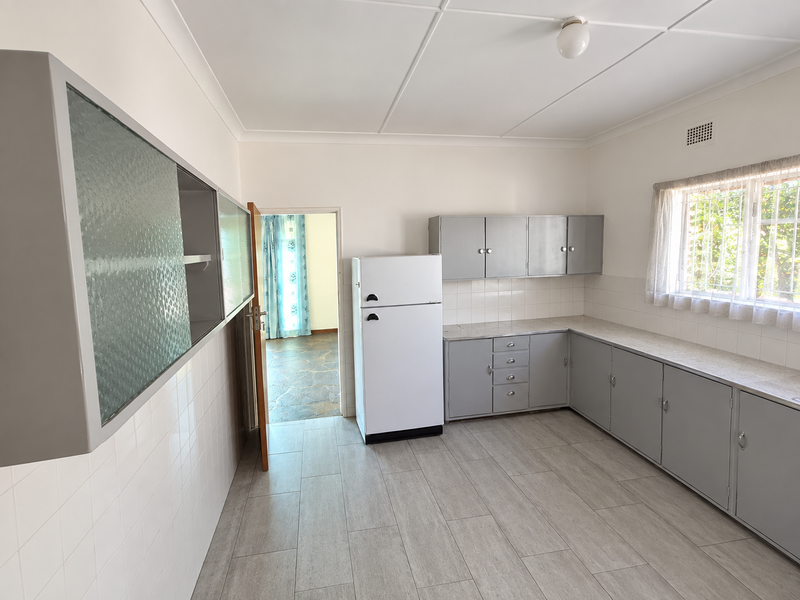 A clean, functional kitchen featuring grey built-in cabinetry, tiled backsplash, and neutral floor tiles, offering a bright and well-maintained space.