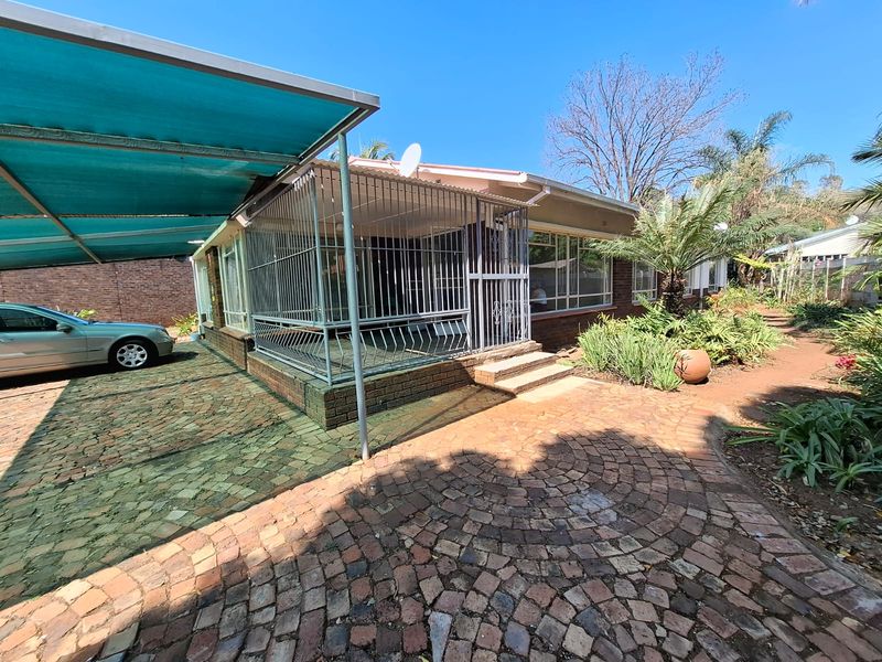 Front exterior view featuring a brick-paved driveway, a covered carport, and a secure entrance area with metal security gates and bars.