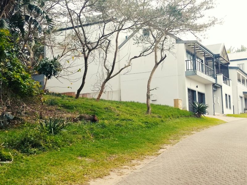 A view of a multi-story residential property featuring a paved driveway, sloped garden area, and balcony, situated in a residential estate.