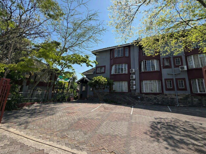 Front exterior view of a multi-story residential building featuring a paved driveway, stone base detailing, and multiple bay windows.