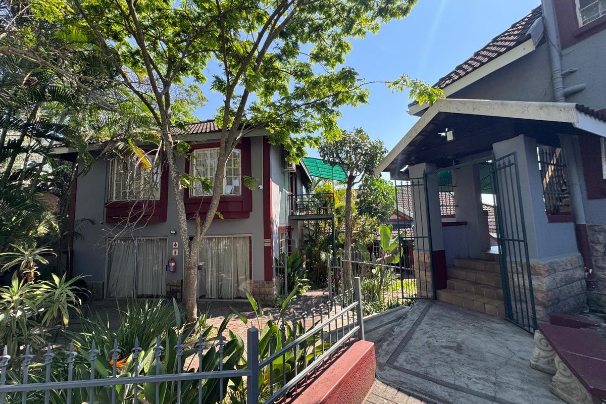 Rear exterior view of the property featuring a paved walkway, concrete stairs, metal security gates, and established garden landscaping.
