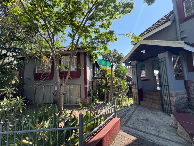 Rear exterior view of the property featuring a paved walkway, concrete stairs, metal security gates, and established garden landscaping.
