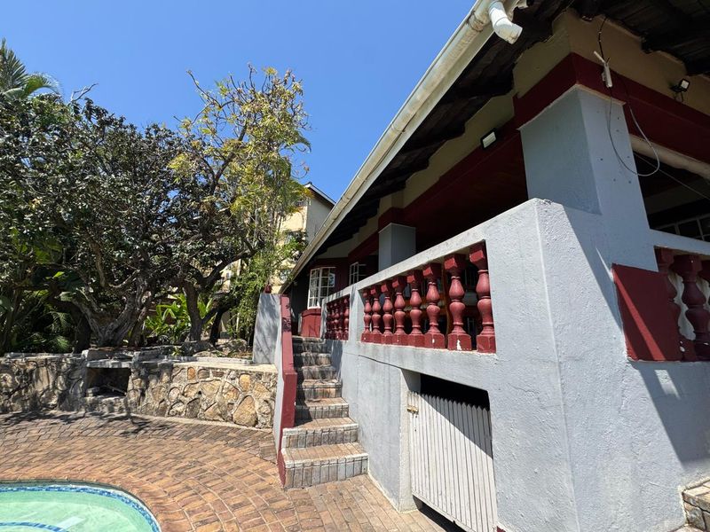 Outdoor pool area featuring a brick-paved deck, stone retaining wall with built-in braai, and a raised patio with concrete balustrades.