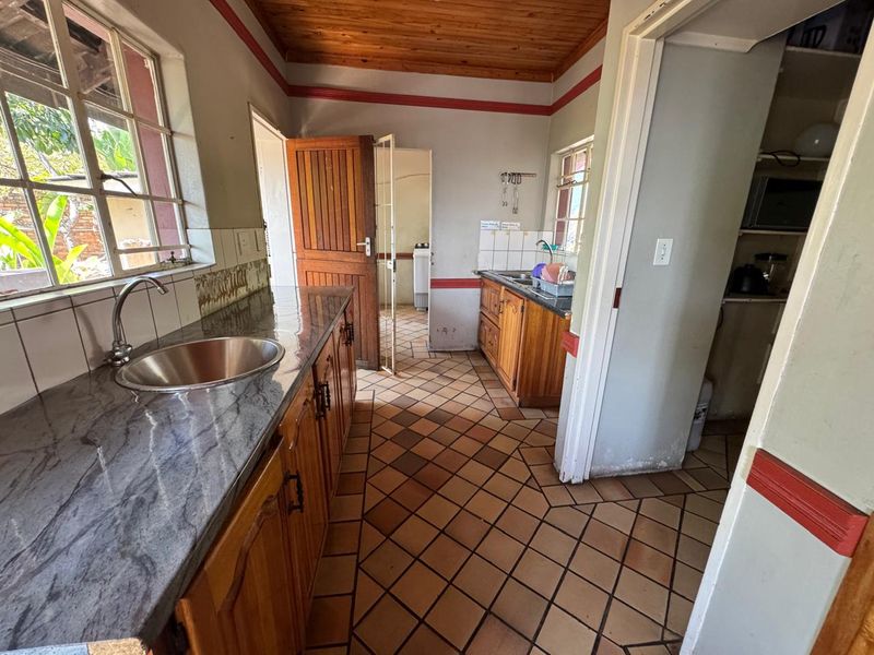 A dated kitchen featuring wooden cabinetry, granite countertops, tiled flooring, and a timber ceiling, offering potential for a modern renovation.