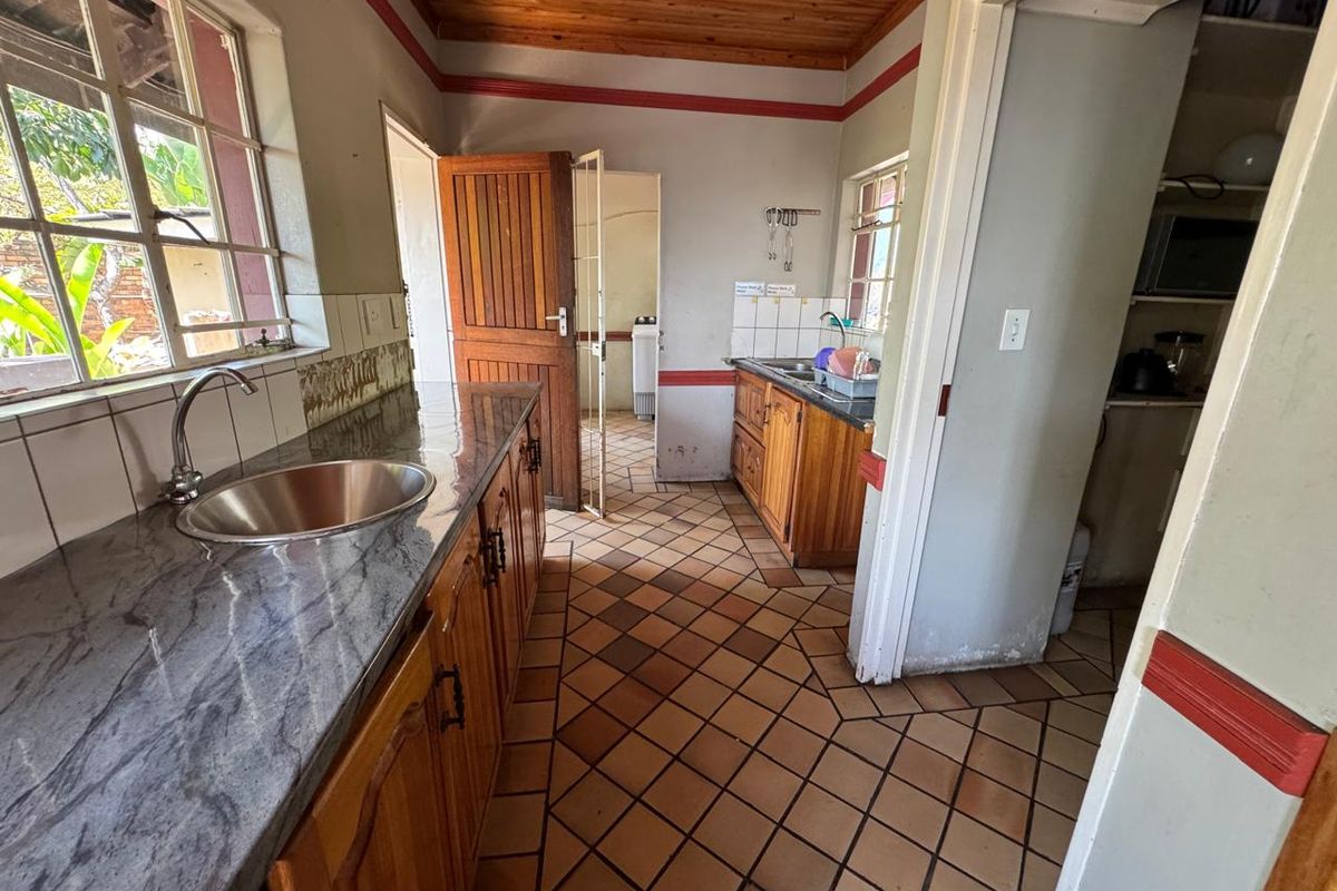 A dated kitchen featuring wooden cabinetry, granite countertops, tiled flooring, and a timber ceiling, offering potential for a modern renovation.