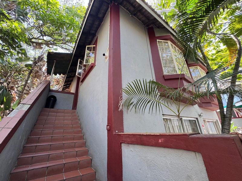 Exterior view of the property featuring a tiled staircase leading to the upper level, bay windows, and established garden surroundings.