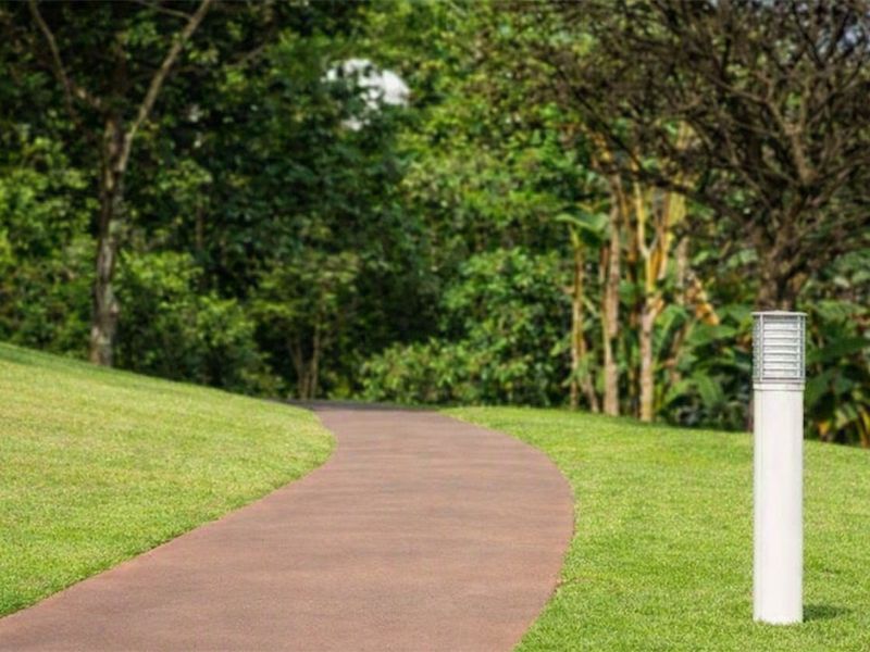 A well-maintained garden area featuring a curved paved pathway and modern bollard lighting set against a backdrop of mature trees.