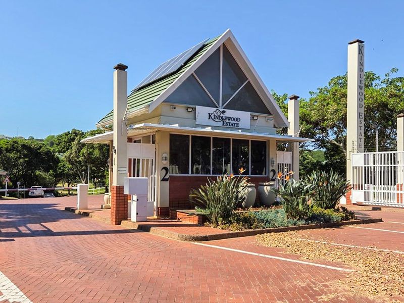 The main entrance gatehouse of Kindlewood Estate, featuring a paved driveway, security boom gate, and solar panels on the roof.